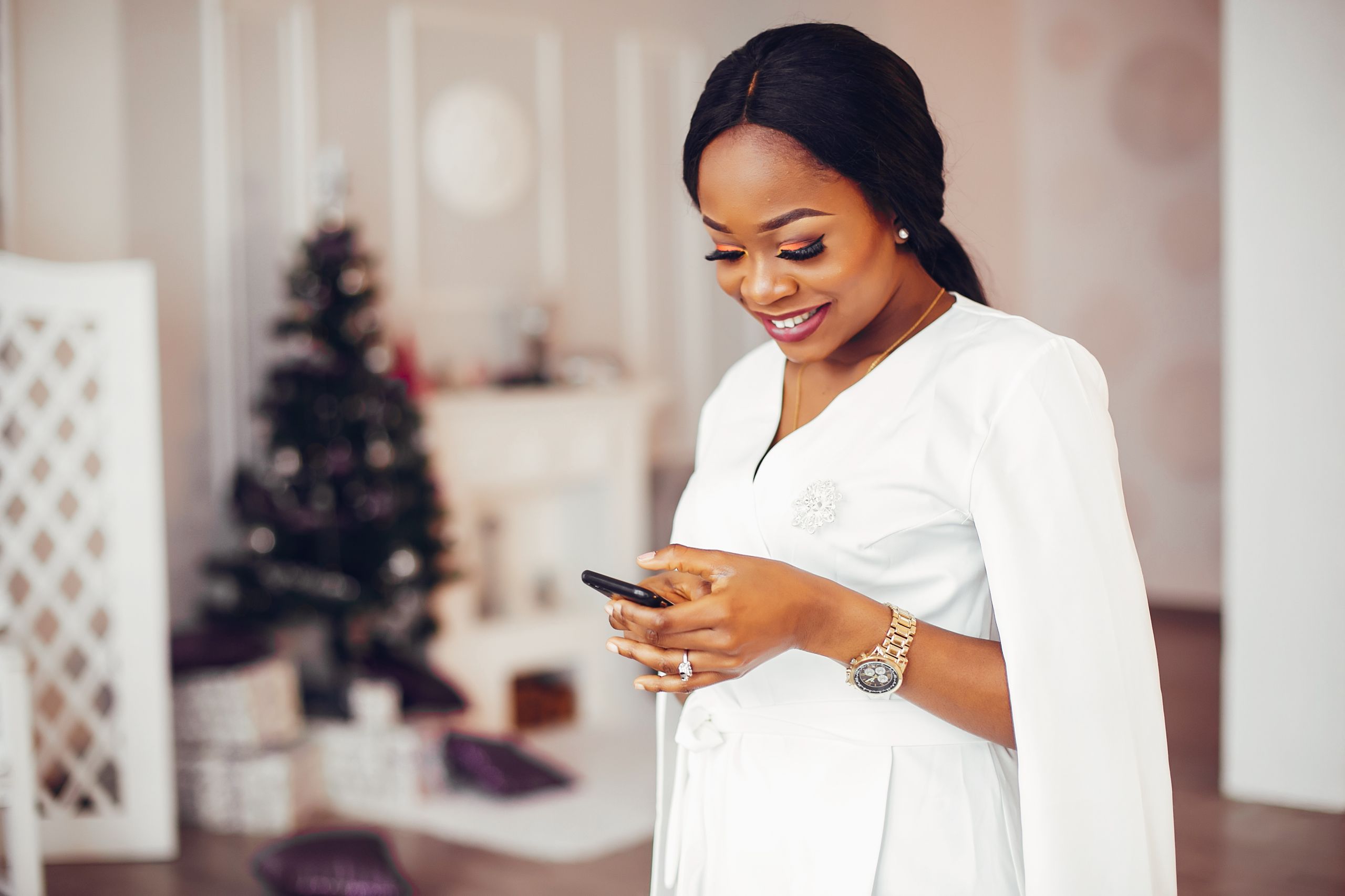 Beautiful girl in a decorated room. Woman use the phone. Black lady in a white dress